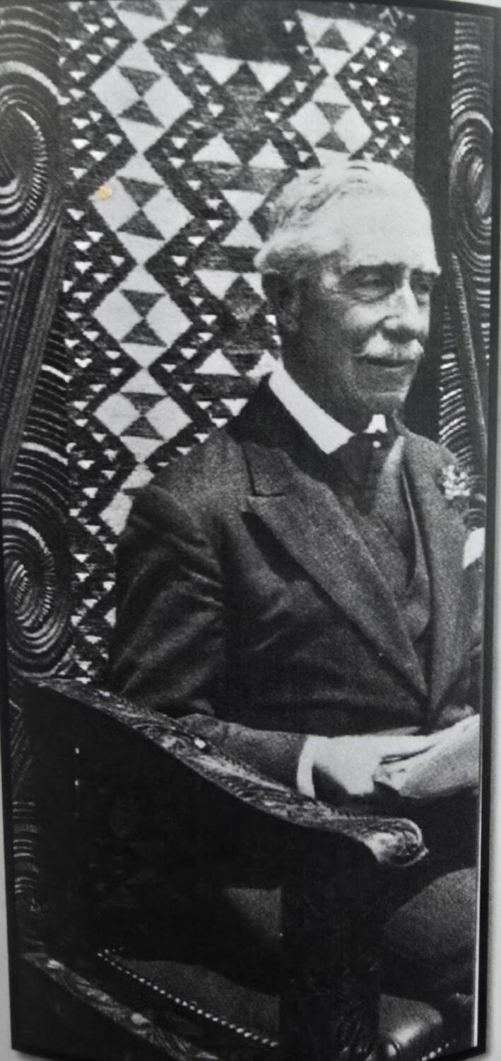 Lord Bledisloe seated in the carved chair, tukutuku panel behind him